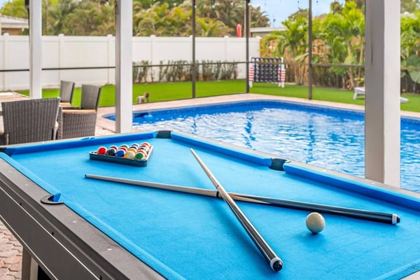 Pool table with cues and balls in screened lanai overlooking swimming pool and manicured lawn