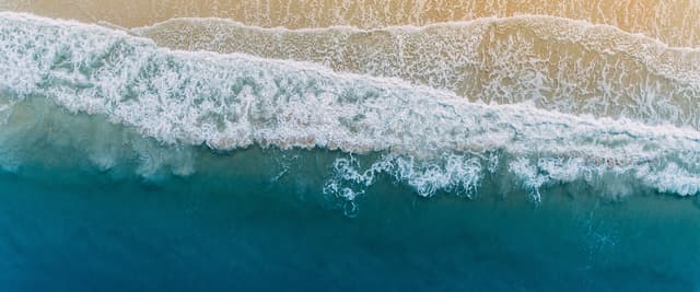 Aerial view of golden sand beach with teal surf and gentle waves